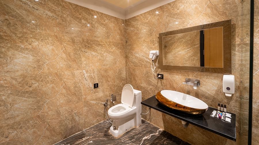Club Room bathroom features a wall-mounted hand wash, hairdryer, a horizontally placed mirror above the wash basin, and a western toilet seat at Crescent Spa & Resort, Indore