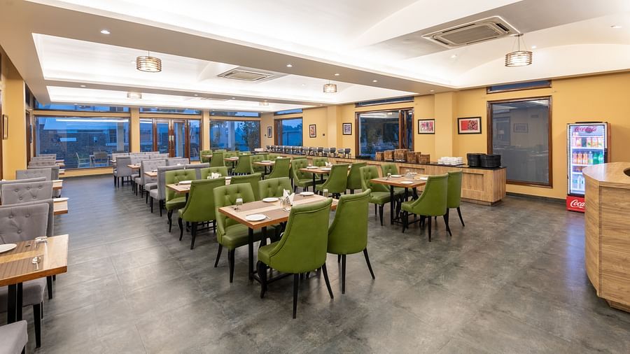 Brightly lit diagonal view of the restaurant at DLS Forest Vines Resort, showcasing tables and seating arranged for guests.