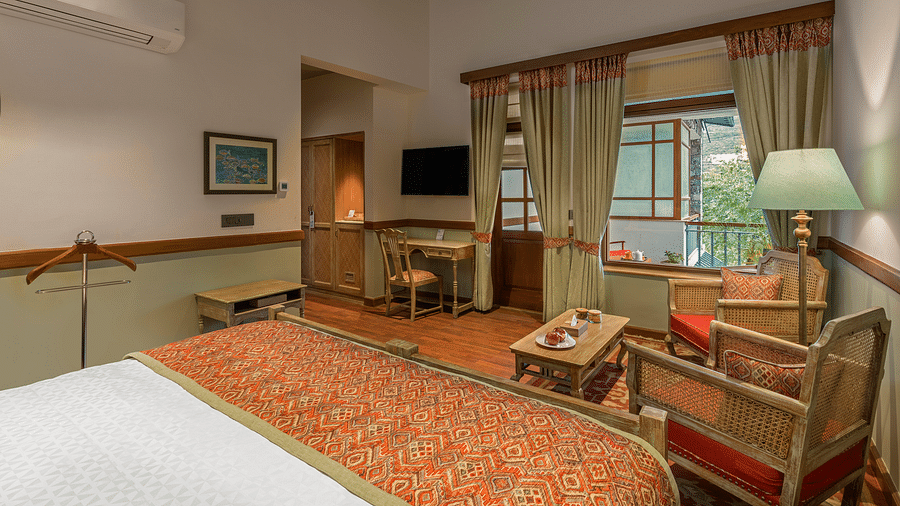 Cozy room at Fishermen's Lodge, Bhimtal, featuring a lamp, TV, chair, tea table, and a beautiful view of the surroundings.