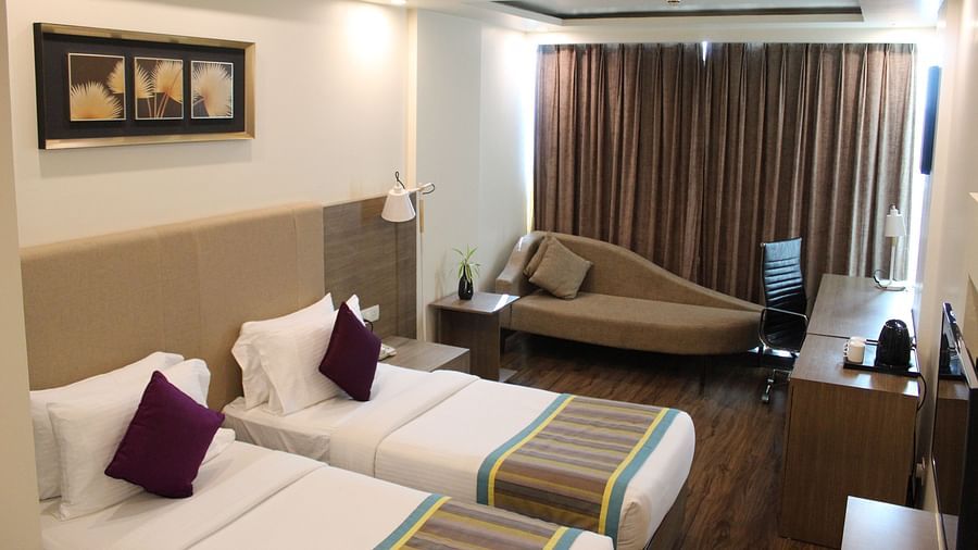 An image showing a pair of twin beds with lush decors, hung artworks, a long sofa with cushion, brightened with lights.