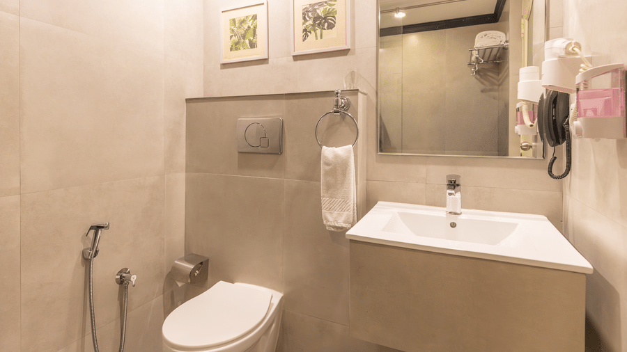 A clean restroom with beige tiles, a large mirror, a white sink, and framed botanical art on the wall at Hotel Horizon, Trivandrum.