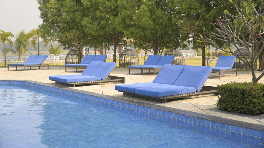 Comfortable blue sun loungers arranged beside the swimming pool under shady trees at Hotel Sonar Bangla, Mayapur.