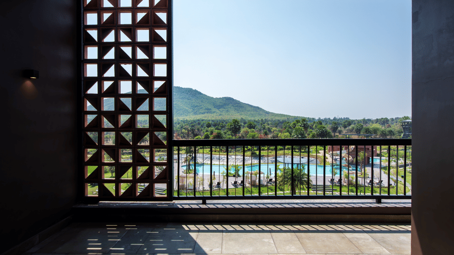 An open balcony view framed by decorative lattice walls overlooking the resort grounds and the scenic Susunia hills in the distance | Hotel Sonar Bangla, Susunia