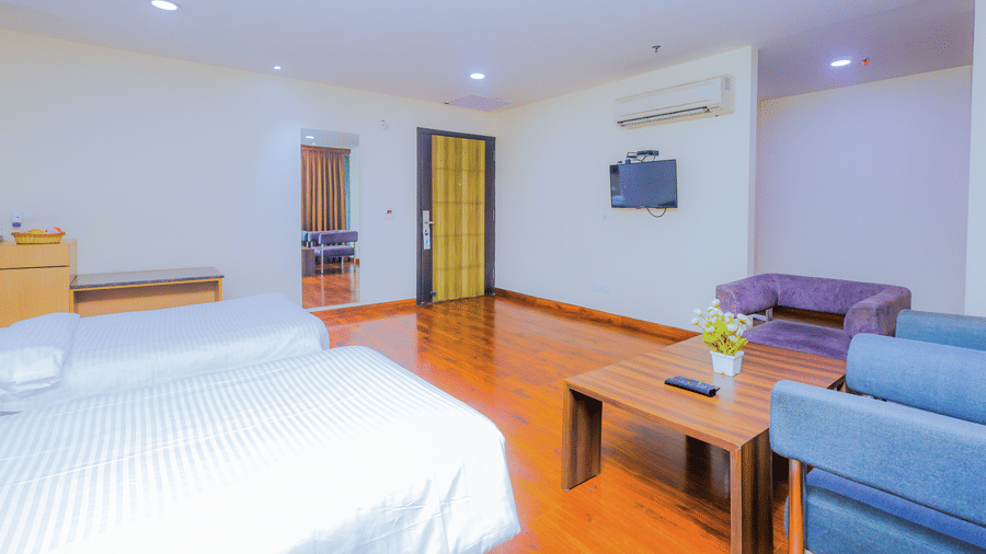 A large hotel suite featuring a bedroom area with a king bed and a separate living area with sofas - Hyphen Business Hotel, Noida