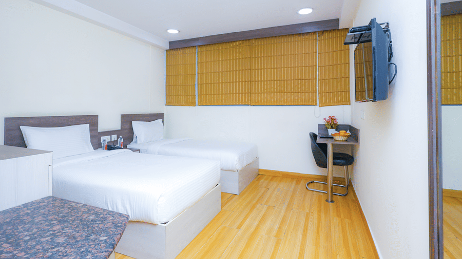 A light filled hotel room featuring a comfortable bed, a small desk, and a television - Hyphen Business Hotel, Noida