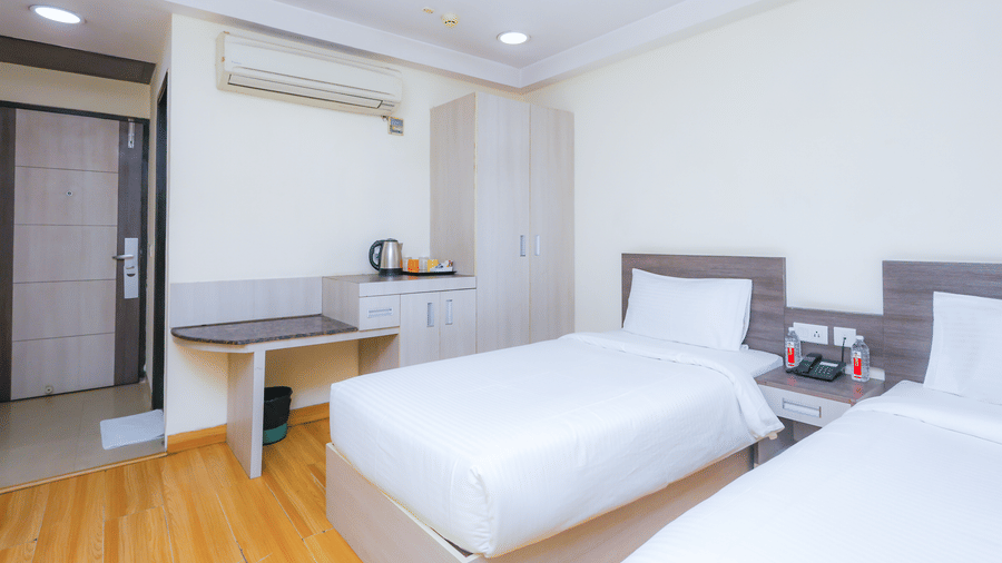 A neat hotel room with 2 single beds, a bedside table, and simple decor - Hyphen Business Hotel, Noida
