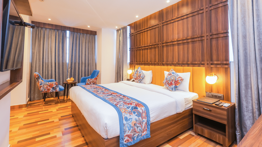 View of a luxurious hotel room with a spacious bed, wooden accents, and a tranquil ambience - Hyphen Business Hotel, Noida
