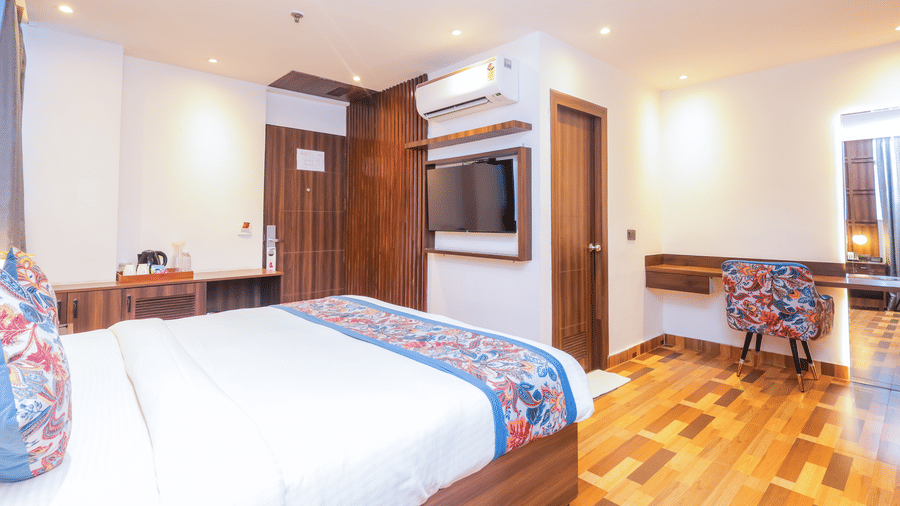 A clean and inviting hotel room featuring a large bed, wooden wardrobe, and a small desk area - Hyphen Business Hotel, Noida