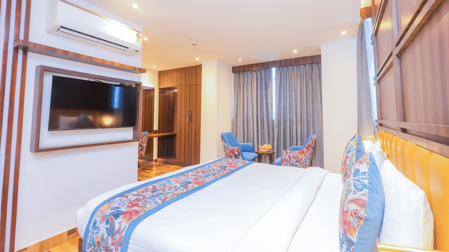 A bright hotel room featuring a comfortable bed, wall mounted television, and a blue armchair - Hyphen Business Hotel, Noida
