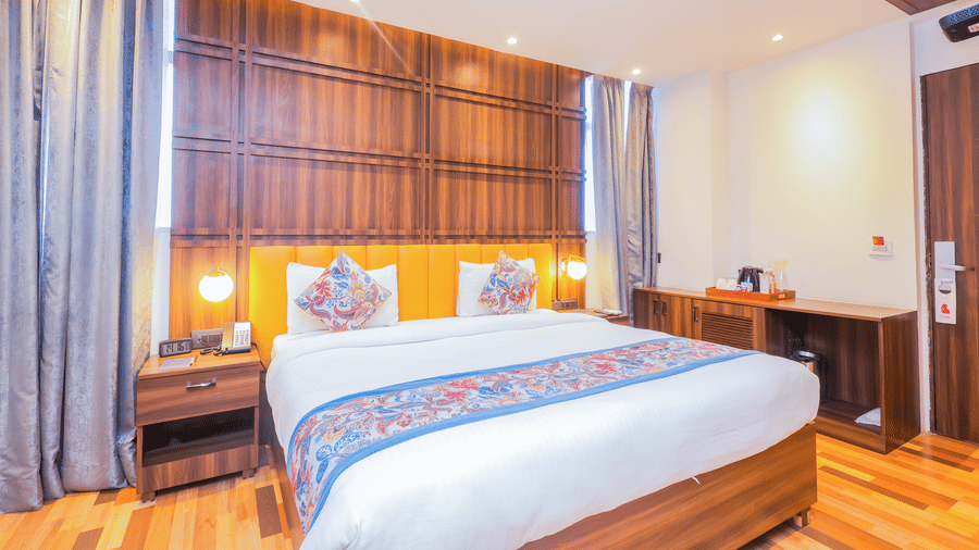 A modern hotel bedroom with a large bed, elegant wooden panelling behind the headboard, and bedside tables - Hyphen Business Hotel, Noida