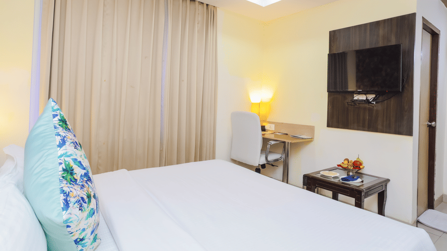 A clean hotel room with a single bed, a wall mounted television, and light curtains - Hyphen Grand, Haridwar