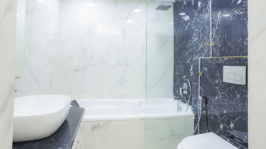 Modern bathroom with a glass shower enclosure, toilet, and sleek white design at Hyphen Premier Hotel, Meerut.