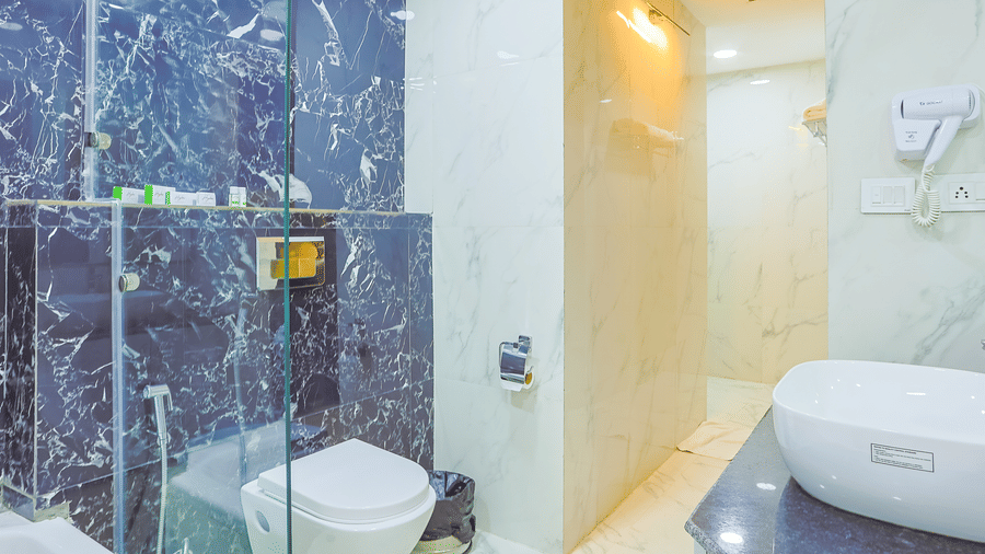 Bathroom featuring blue marble tiles, glass shower partition, and compact toilet setup at Hyphen Premier Hotel, Meerut.