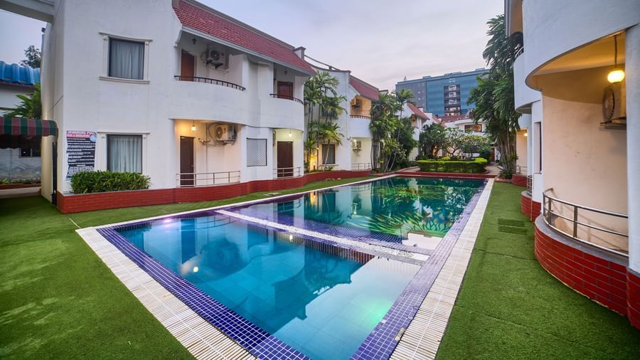 Wide exterior view of the hotel building overlooking a sparkling blue swimming pool surrounded by green lawn at Ilara Hotels & Spa, OMR, Chennai.