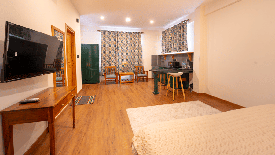 A bright living space with a wall-mounted flat-screen TV, wooden console, and warm lighting - Johnson Lodge & Spa, Manali