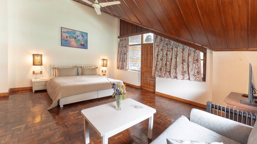 A spacious premium attic bedroom with polished wooden floors, white furniture, and a high timber-lined ceiling - Johnson Lodge & Spa, Manali