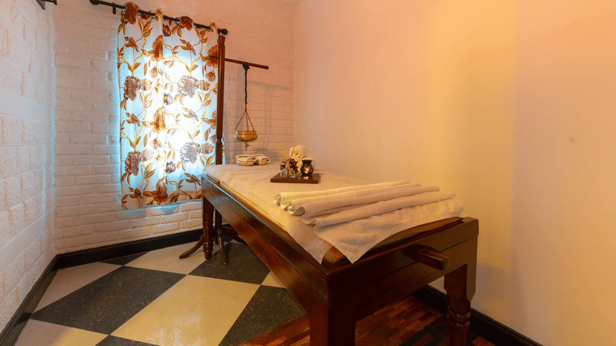An intimate massage room featuring a wooden therapy bed and checker stone flooring - Johnson Lodge & Spa, Manali