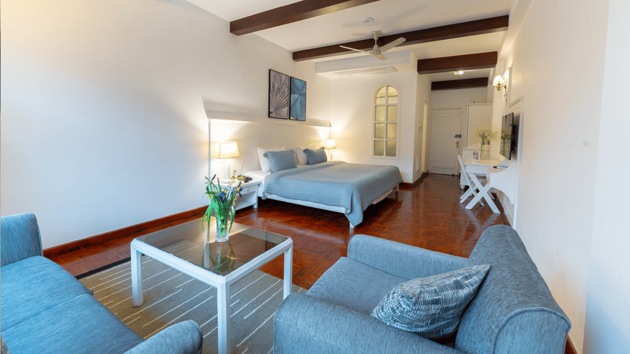 A wide-angle view from the living area toward the bed, showcasing the open-plan layout and wooden accents - Johnson Lodge & Spa, Manali