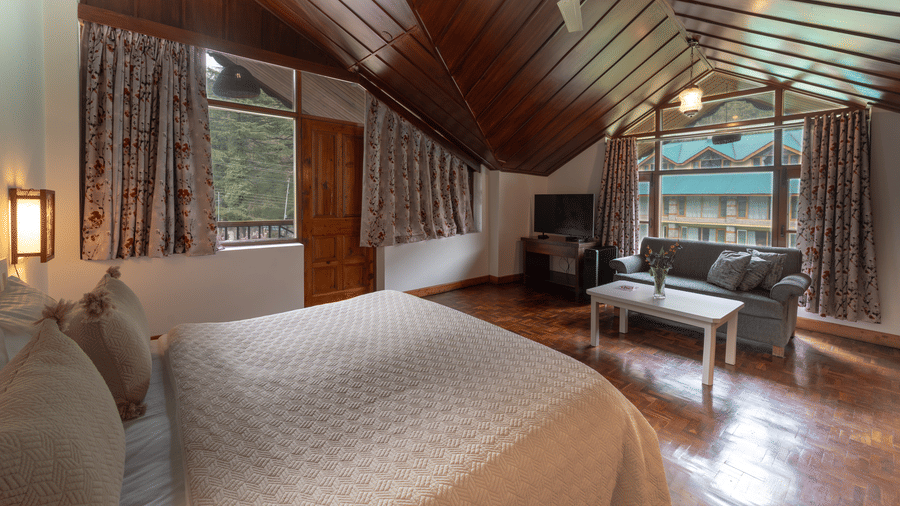 A perspective of a guest room highlighting the warm wood panelling on the slanted ceiling and large windows - Johnson Lodge & Spa, Manali