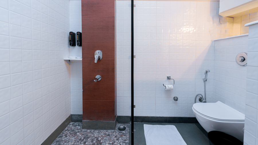 A modern bathroom featuring a walk-in shower with dark pebble flooring and white tiled walls - Johnson Lodge & Spa, Manali
