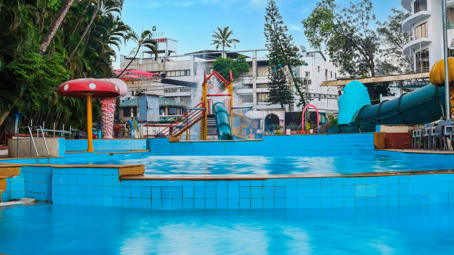 View across the clear swimming pool area toward the resort buildings and multiple water slide exits at Kumar Resort by Turtle.