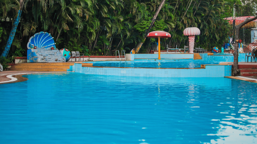 A section of the outdoor pool area surrounded by dense tropical foliage and small, themed shade structures at Kumar Resort by Turtle.