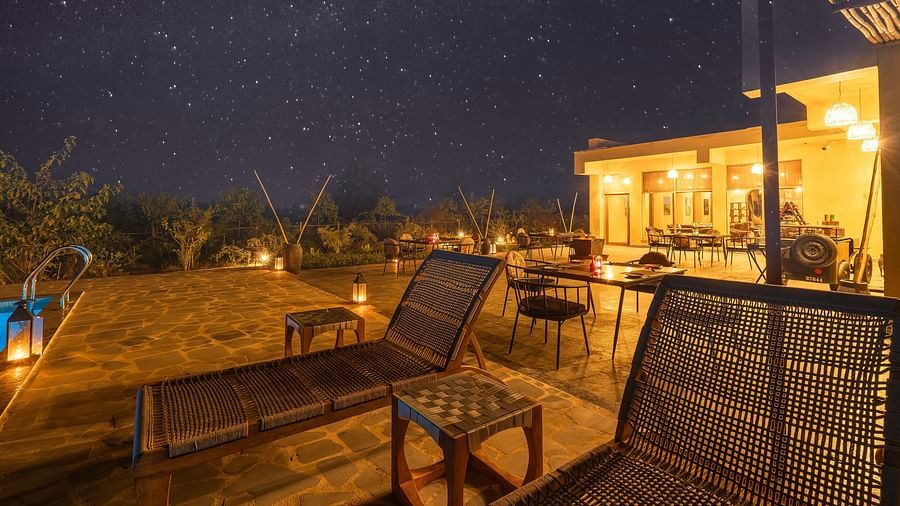 An image of Rosette restaurant at night time featuring wooden lounger beds, stools, tables and chairs, a swimming pool, and a huge patio - Kurja Jawai