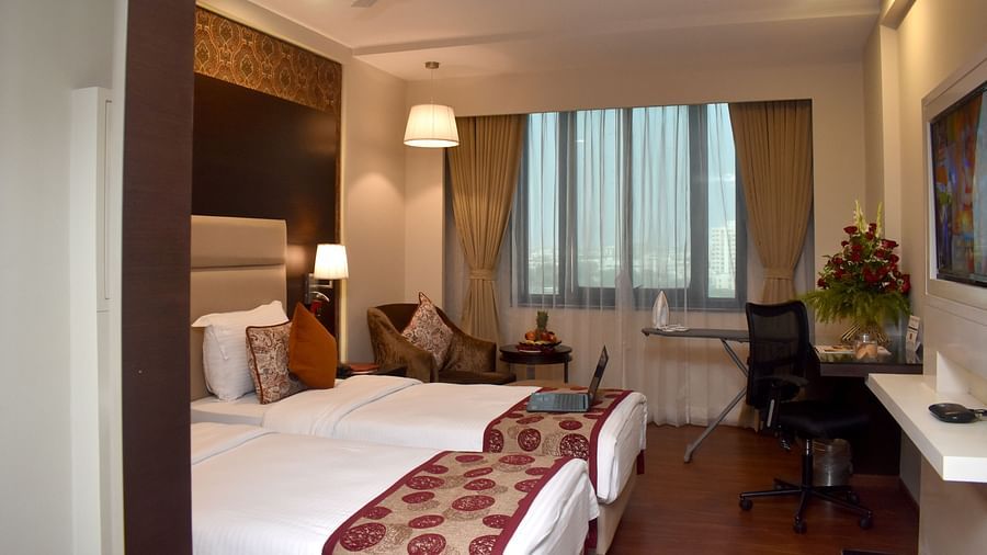 A well-lit hotel room features two beds and comfortable furnishings at Lords Plaza Surat.