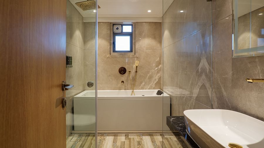 A well-lit bathroom features a white bathtub, a toilet, and a mirrored wall reflecting the fixtures and neutral-toned tiles - Melior Inn