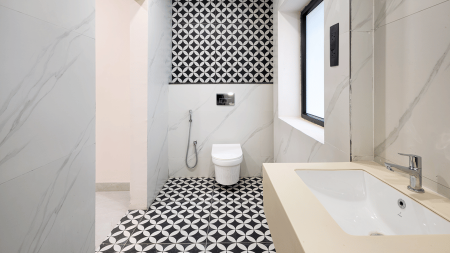 A bathroom featuring a white sink basin, a flush toilet, and patterned black-and-white floor tiles at Monday Hotels & Suites Madhapur Hyderabad.
