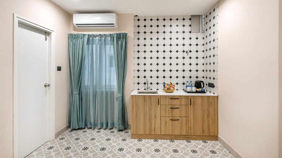 A room including a small kitchenette with wooden cabinets, a sink counter, and a doorway next to curtains at Monday Hotels & Suites Madhapur Hyderabad.