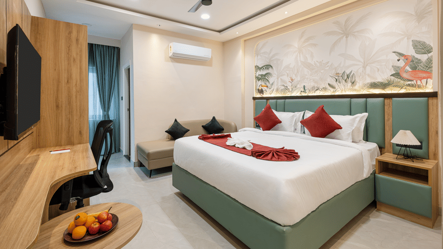A bedroom with a doubking sizele bed decorated with red pillows, a ceiling fan, side tables, and a work desk at Monday Hotels & Suites Madhapur Hyderabad.