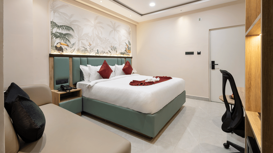 A bedroom containing a king size bed with red accent pillows, a couch, a ceiling fan, and a desk area at Monday Hotels & Suites Madhapur Hyderabad.