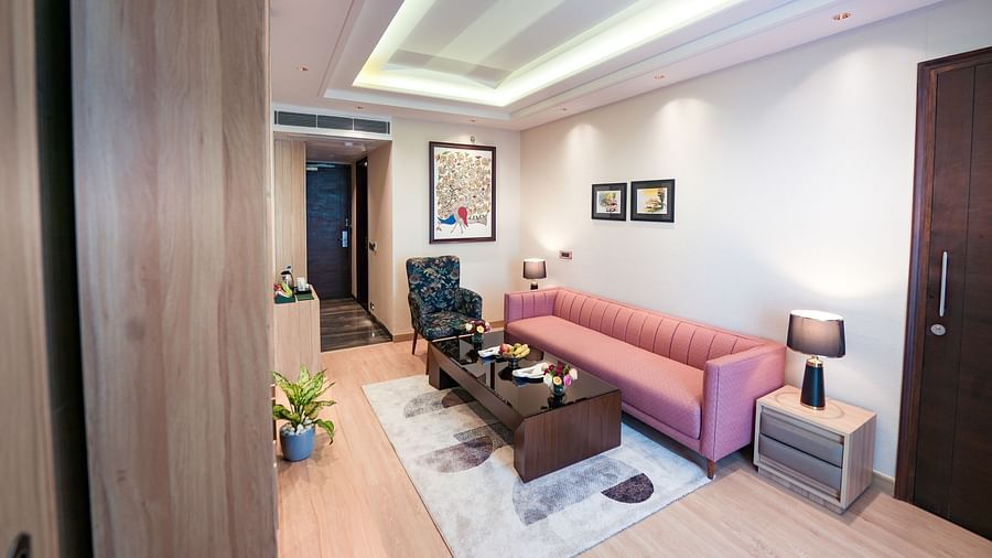 A living area in our Executive Suite featuring a large pink couch, with night lamps placed on either side of the coffee table and paintings hanging on the walls - NAMAMI BY ZENQ BANKHANDI