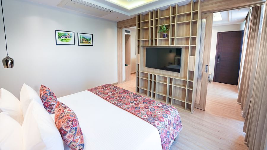 A bed in our suite featuring a floral-patterned bed runner and pillows, positioned in front of a wall-mounted television - NAMAMI BY ZENQ BANKHANDI