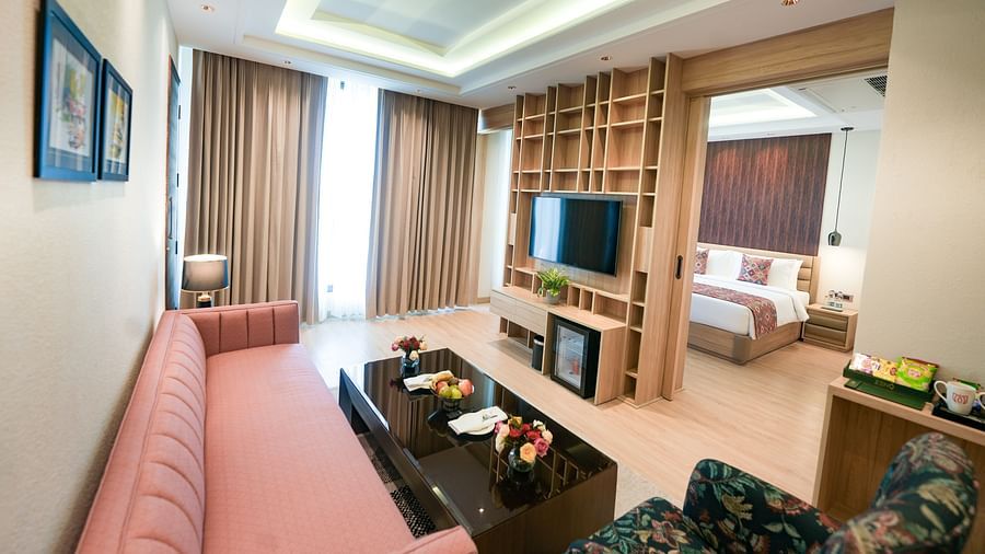 An image showcasing our expansive Executive Suite, featuring cosy furniture, a wall-mounted television, a minibar in the foreground, and a large bed in the bedroom at the back - NAMAMI BY ZENQ BANKHANDI