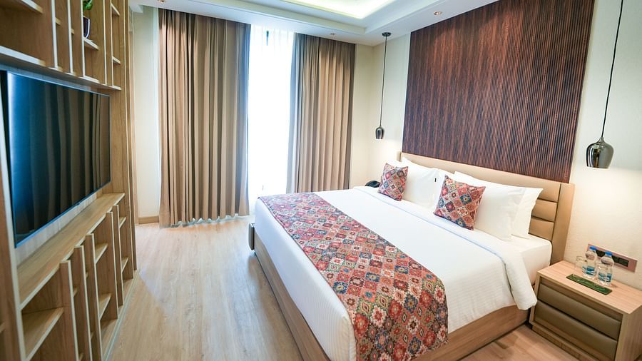 An image of a queen size bed adorned with a floral-patterned bed runner, positioned in front of a wall-mounted television - NAMAMI BY ZENQ BANKHANDI
