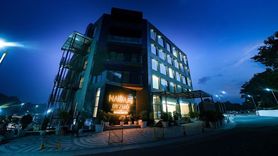 A hotel building set against a dark sky, illuminated by the brightly lit signage displaying the name of the hotel - NAMAMI BY ZENQ BANKHANDI