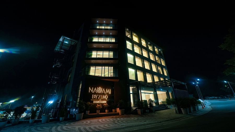 A nighttime image of the facade of a hotel building in Kangra, with bright lights illuminating its details and signage glowing with warm lighting - NAMAMI BY ZENQ BANKHANDI