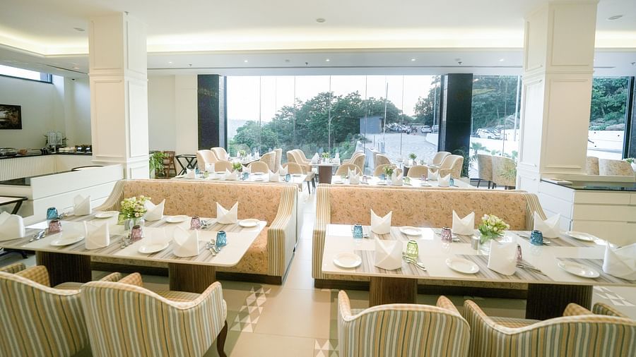 NUTMEGG restaurant in Bankhandi features large tables in front of floor-to-ceiling windows, offering views of the surrounding lush greenery - NAMAMI BY ZENQ BANKHANDI
