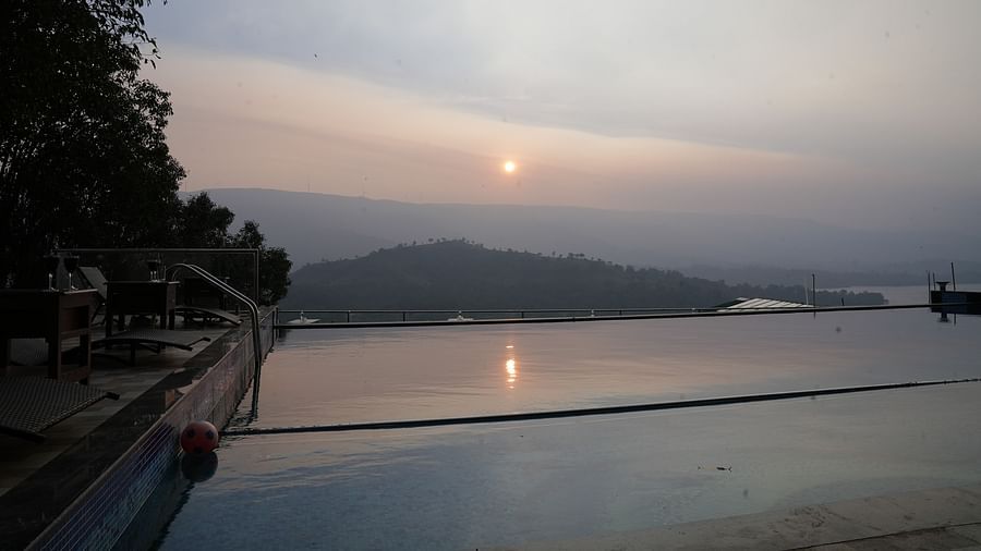 An image of the infinity waterfall swimming pool with the backdrop of the mountains and the setting sun - Nisarga Lake Resort