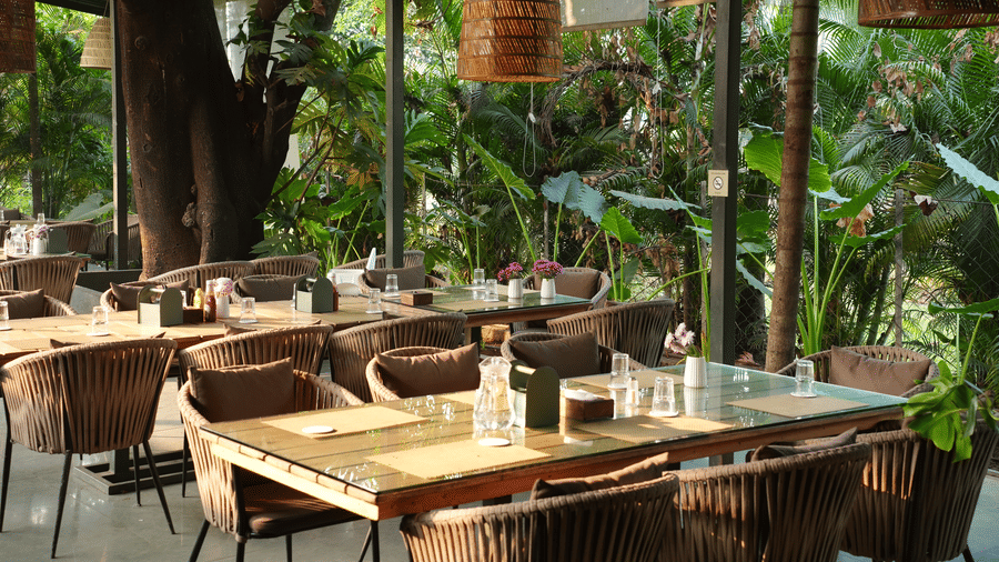 An outdoor dining area at Oceanature Resort, Alibaug with tables and chairs set up under a covered roof with woven lamps.