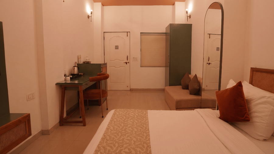 A bedroom with a queen size bed, a wardrobe along the wall, a small desk with a chair, and full-length mirrors.