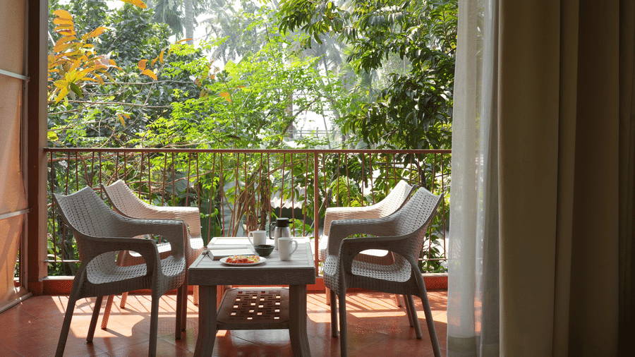 An outdoor balcony at Oceanature Resort, Alibaug featuring 4 chairs and a small table overlooking green trees.