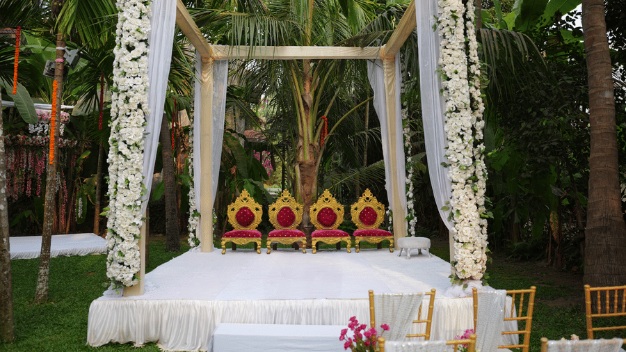 A white outdoor stage structure decorated with hanging white flowers and 4 red-and-gold chairs at Oceanature Resort, Alibaug.