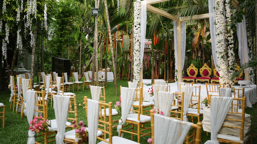 Rows of chairs face a white wooden stage decorated with draped flowers on an outdoor lawn at Oceanature Resort, Alibaug.