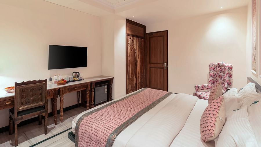 A spacious bedroom view from the headboard at Panna Vilas Palace, showcasing a wall-mounted television with a wooden table positioned below it