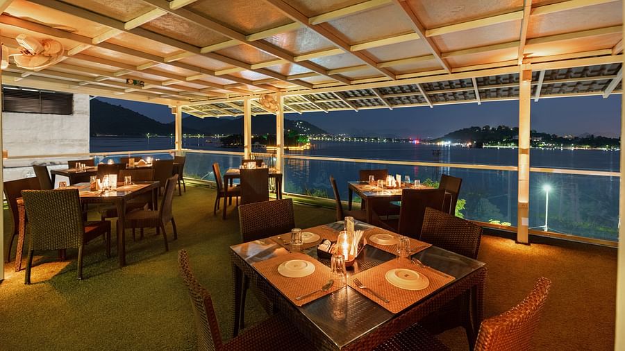 Restaurant area at Panna Vilas Palace features a four-seater table surrounded by wooden chairs, beautifully illuminated by warm lighting, creating an inviting night view - Panna Vilas Palace, Udaipur
