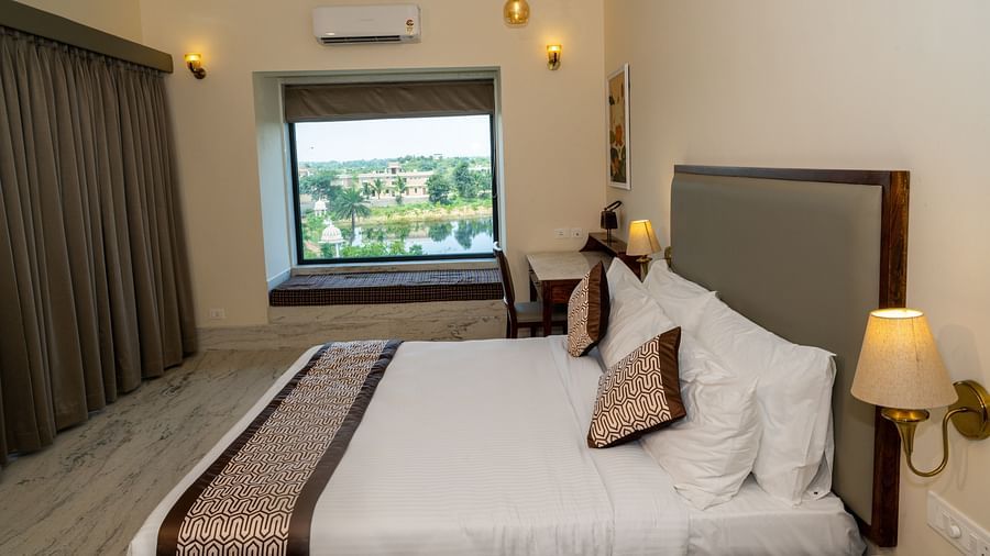 A room with a double bed, night lamps and a window overlooking lush greenery - Rajbagh Wellness, Udaipur