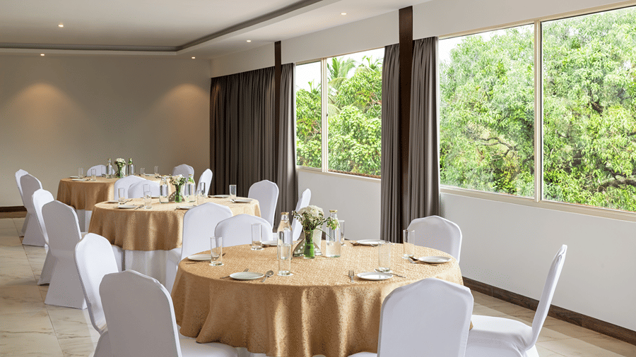 Bright banquet hall arranged with round tables and chairs beside large windows.